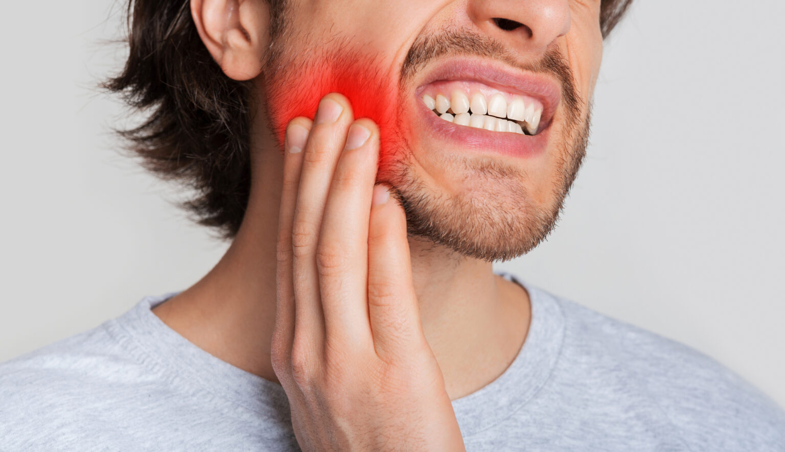 Tooth and gum inflammation. Guy suffers from pain in his mouth and presses hand to red sore spot, panorama, cropped, studio shot